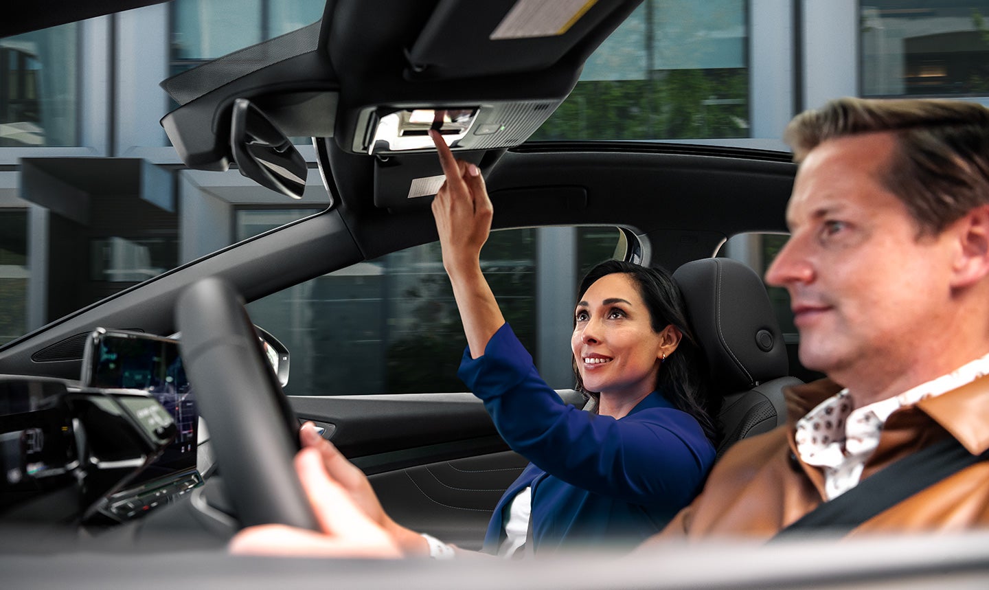 A man and woman sit in the front seats of an ID.4 AWD Pro S Plus. The woman in the passenger seat is reaching up to the overhead console for the switch button to open the sunshade.